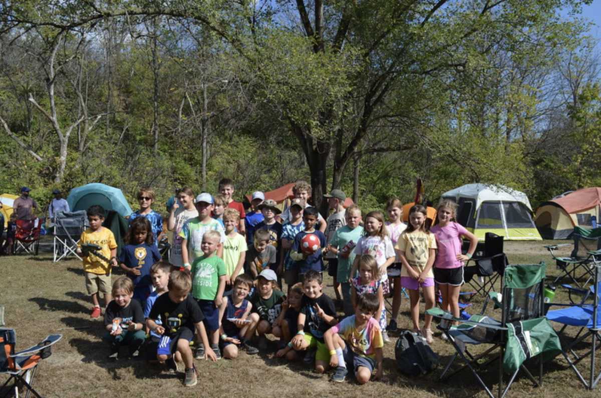 A bunch of scouts smile at the camera, surrounded by tents
