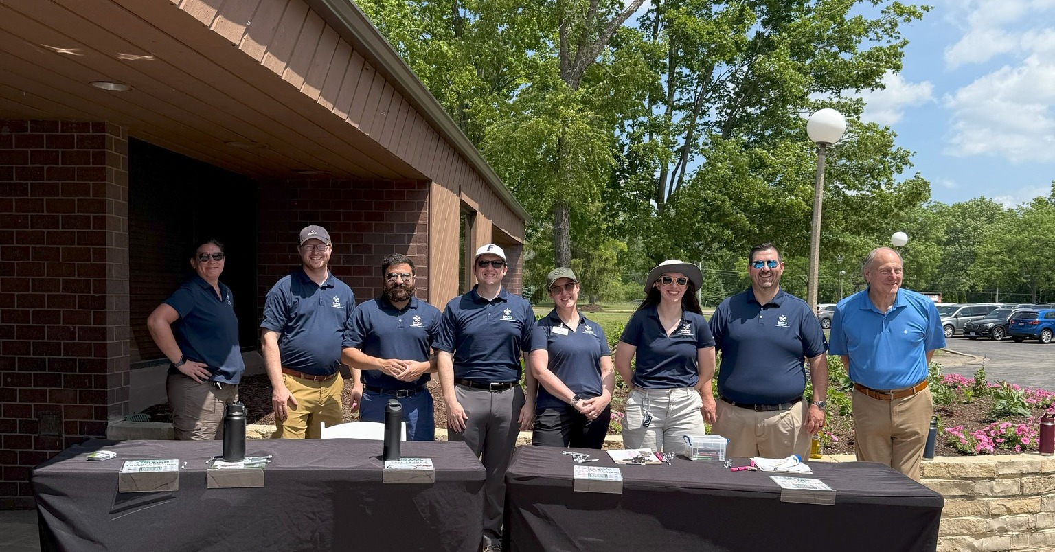 A team of people wearing matching NEIC-branded shirts stand ready to welcome members to the Golf Classic event